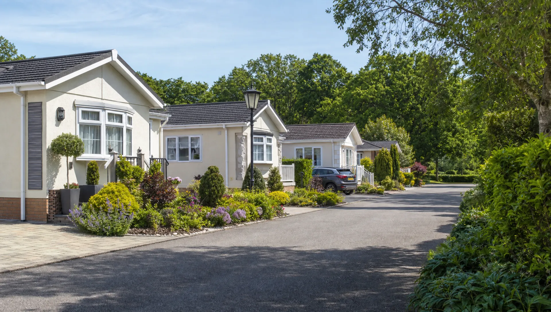 A quiet private residential park in Berkshire with detached luxury park home bungalows, neat gardens, driveways and mature planting along a calm lane.